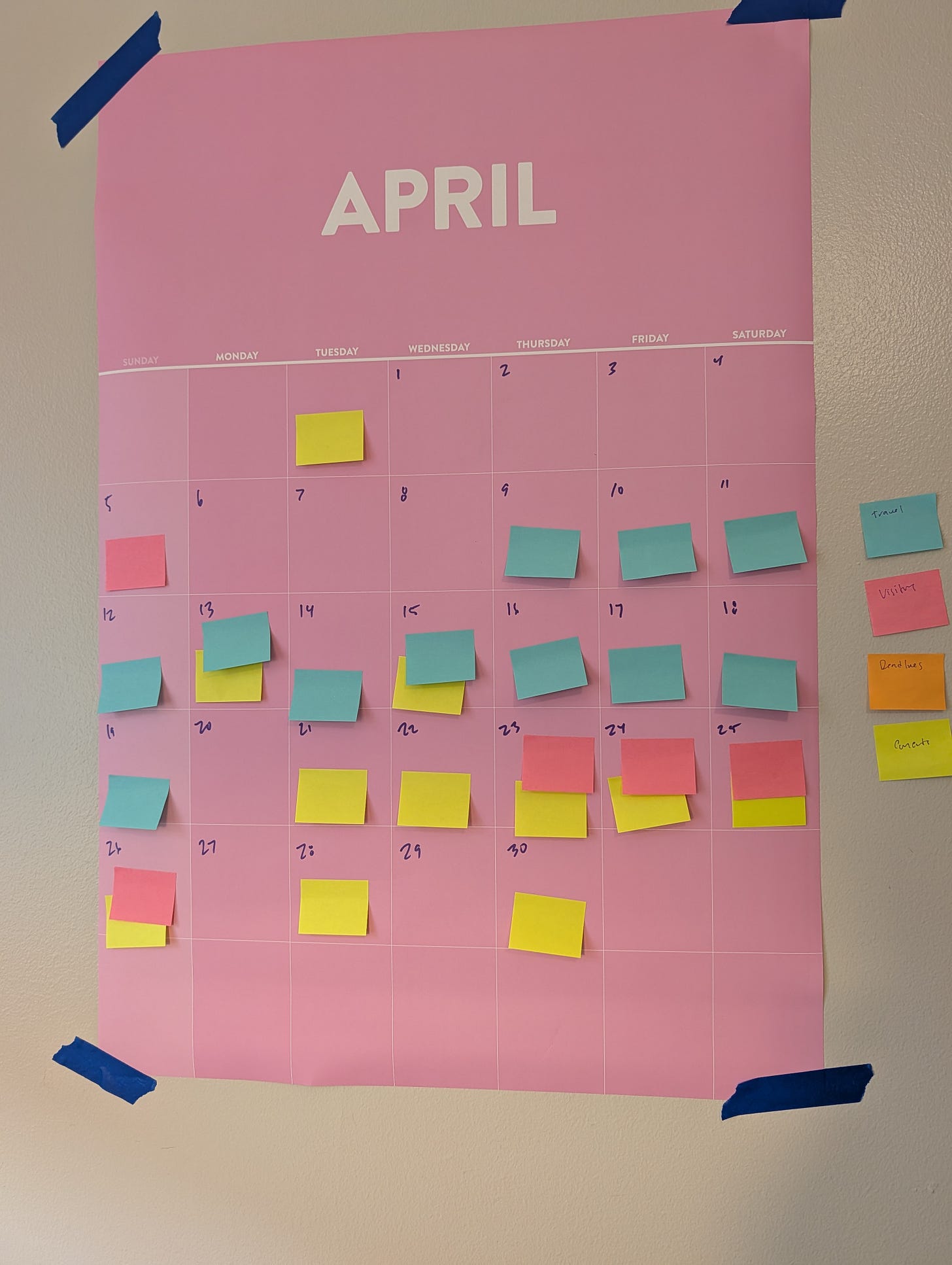 Alt text: a big ass pink April calendar taped to the wall with painter’s tape that has yellow, blue, and pink post-its on it. Alt text: a big ass pink April calendar taped to the wall with painter’s tape that has yellow, blue, and pink post-its on it.