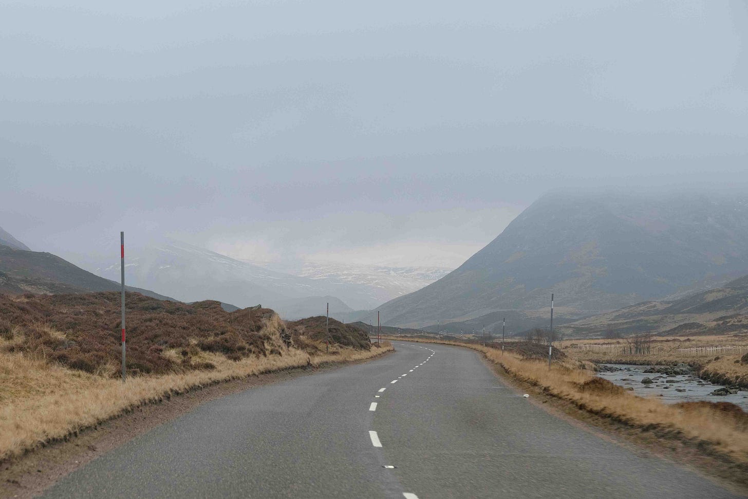 A winding road fades off into distant moutains through a narrow opening in the clouds. 