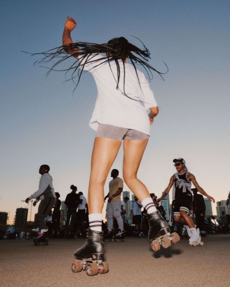 This may contain: a woman riding a skateboard down a street next to other people on rollerblades