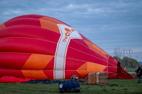 Înainte ca baloanele să urce, totul începe jos, pe iarbă, în frigul subțire al dimineții sau în lumina care abia se stinge peste câmp. Oamenii își ocupă locurile, verifică arzătoarele, întind pânza, ridică nacela, privesc cerul și, mai ales, ascultă vântul. În jur, mașinile stau cu farurile aprinse.
