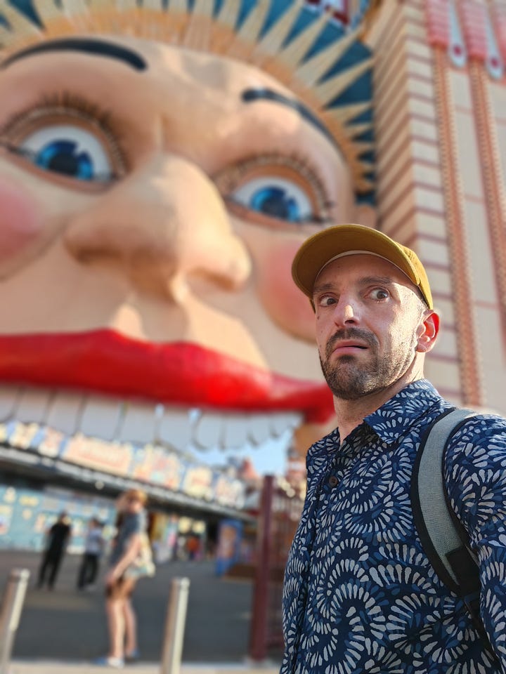 1. A view of a cove with houses around it and boats in the water. 2. An ibis lingering by a blonde man eating a sandwich. 3. The multi-layered strawberry watermelon ice cream. 4. A man looking humorously scared in front of the Luna Park entrance, depicting a giant grinning face.