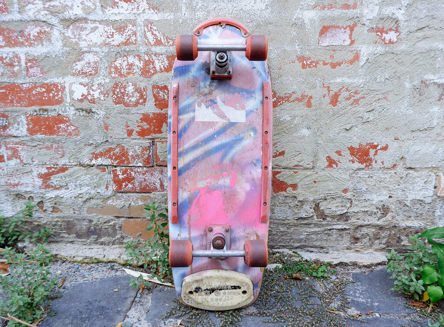 An old pink skateboard leaning against a wall An old pink skateboard leaning against a wall