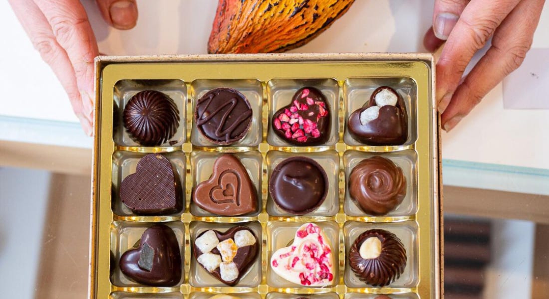 A gold box of chocolate with chocolate truffles in it, being held by hands on a counter A gold box of chocolate with chocolate truffles in it, being held by hands on a counter