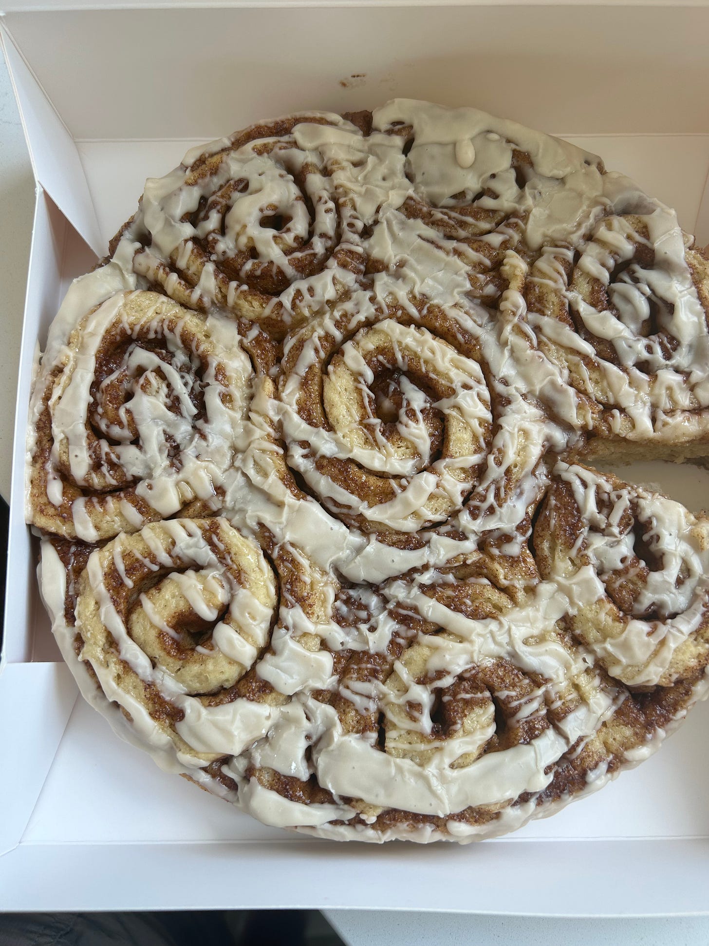A round of iced gluten-free cinnamon rolls in a white bakery box, one roll missing.