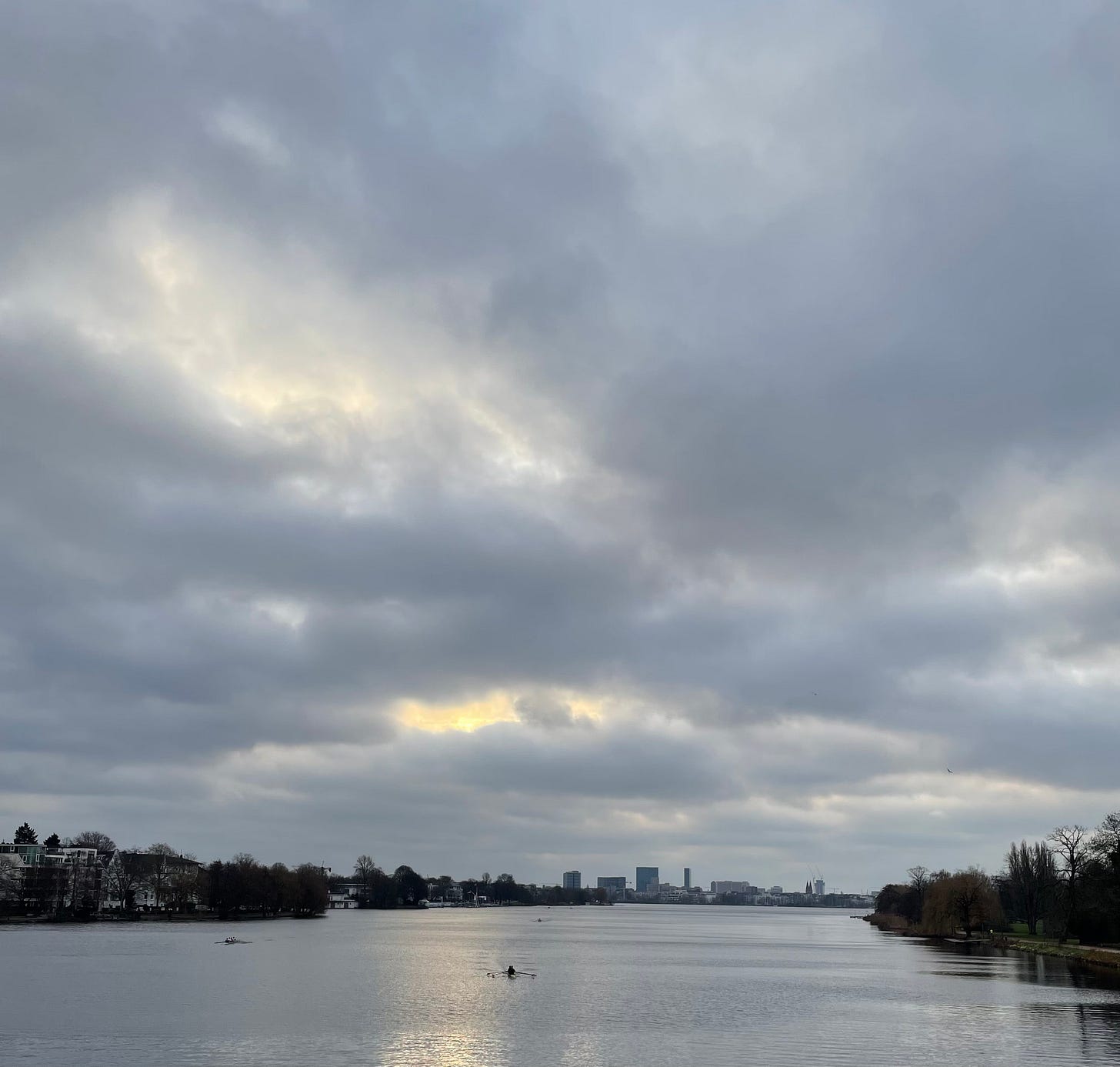 View over the Alster river with a tiny sliver of sunshine peeking through gray clouds.