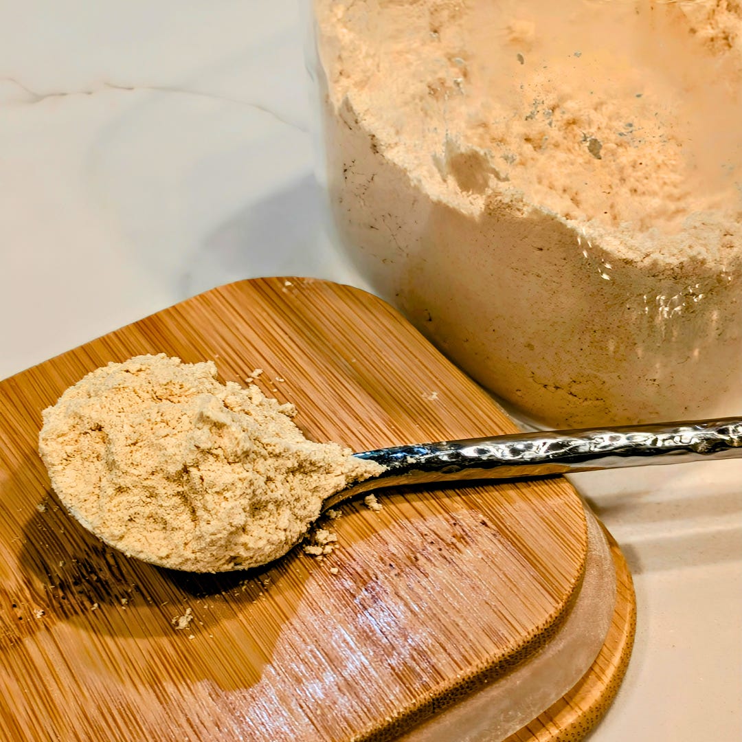 Close-up of kinako, roasted soybean flour, with a spoonful resting on a wooden board beside a large jar.