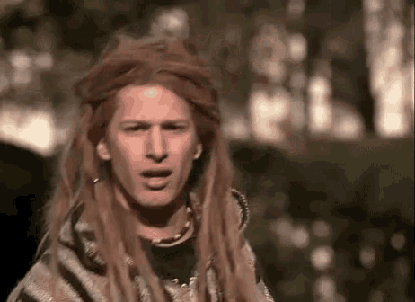 a man with long hair and dreadlocks is wearing a poncho and making a face .