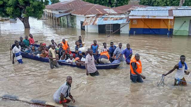 A flooded street with a boat full of people being guided by others who are wading in the water A flooded street with a boat full of people being guided by others who are wading in the water