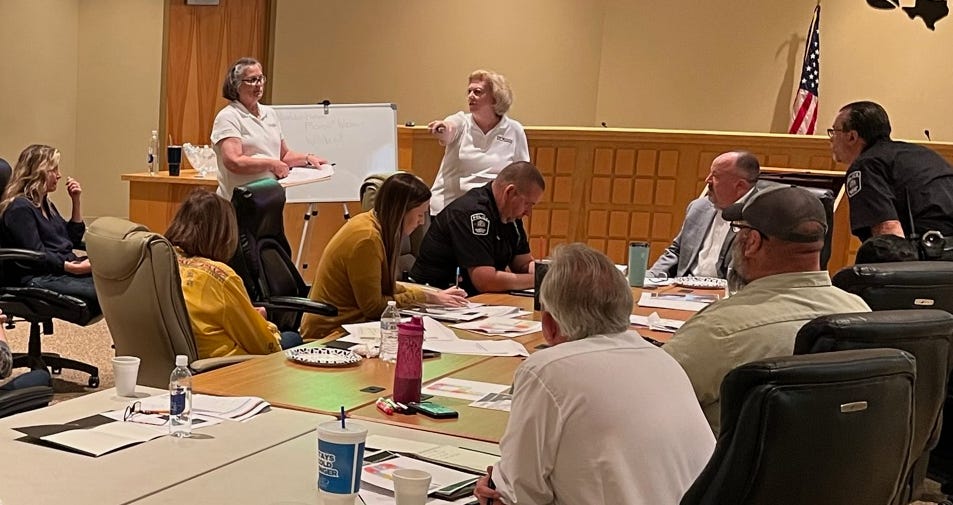 Belinda Willis stands at the front of a conference room, gesturing while speaking to city staff and public safety leaders during a tabletop crisis communication exercise facilitated by DFW StratComm.