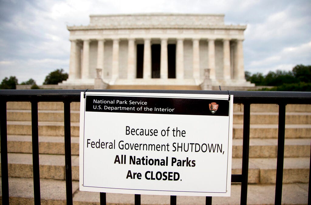 A sign posted in front of a stone monument reads "Because of the federal government shutdown all national parks are closed."