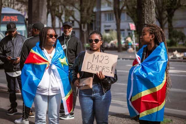 Demonstrators draped in flags hold up a placard -- which reads "M23 OUT" in French Demonstrators draped in flags hold up a placard -- which reads "M23 OUT" in French