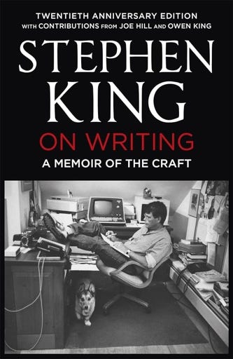 The 2020 edition cover of On Writing by Stephen King. Beneath the title is a photo of King in his office with his feet up on the desk as he writes on a legal pad. Computer and writing equipment litter his surroundings, and his corgi Marlow walks out from under King's legs.