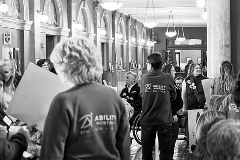 A gallery of black and white photos of a rally in the rotunda of Montana's state capitol. people are holding signs in support of disability rights, there is a podium with legislators speaking, people with a virety of physical disabilities are throughout the crowd.