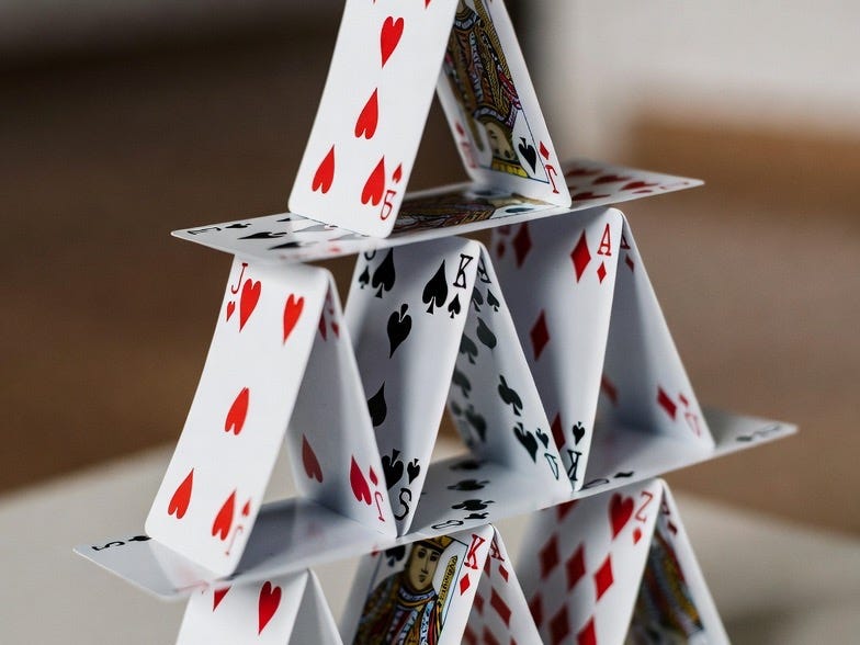 A photograph of a precarious house of cards on a smooth surface, in a blurred indoor setting. A photograph of a precarious house of cards on a smooth surface, in a blurred indoor setting.
