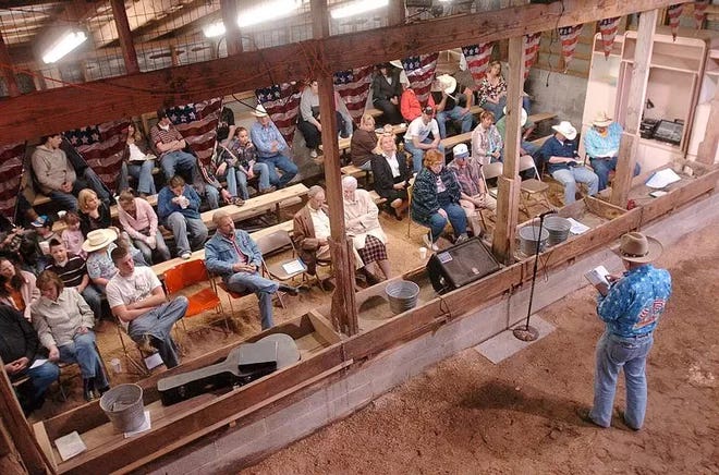 Cowboy Church showing congregation facing toward camera with a preacher in a cowboy hat standing on sawdust, apparently in a barn