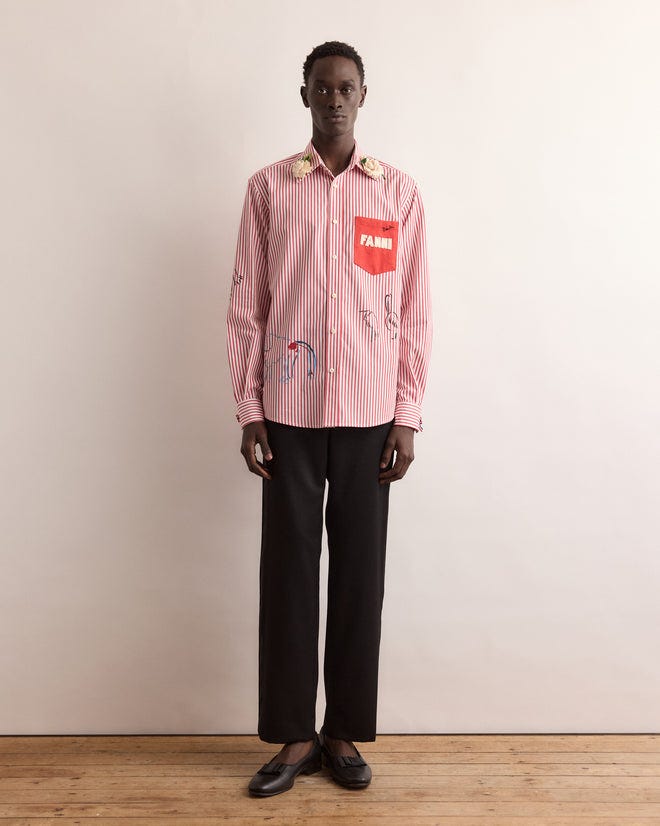 Someone wearing a Calder Painted Cirque Long Sleeve Shirt with designs and black pants stands against a plain background.