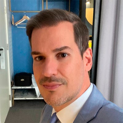 Homem de terno. Ele aparenta estar em um escritório