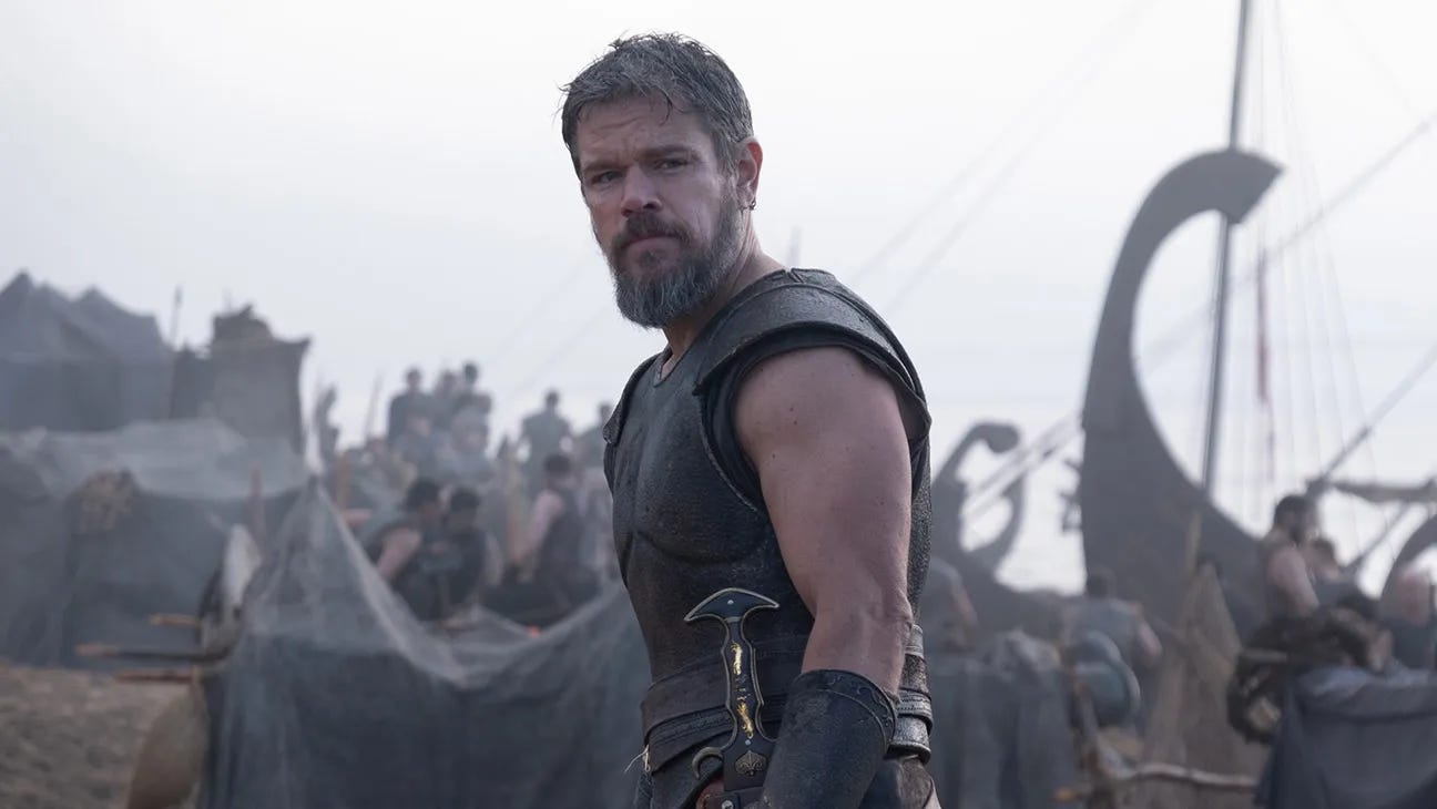 Movie still from The Odyssey. Matt Damon looks offscreen, his army of men in the background by his boat.