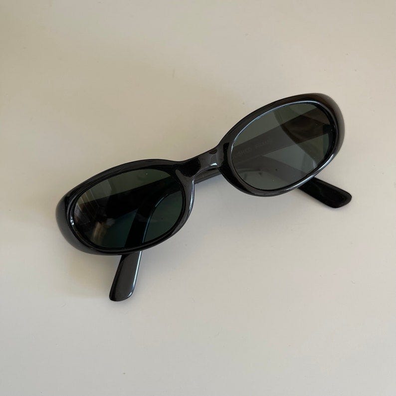 May include: Black oval sunglasses with dark lenses