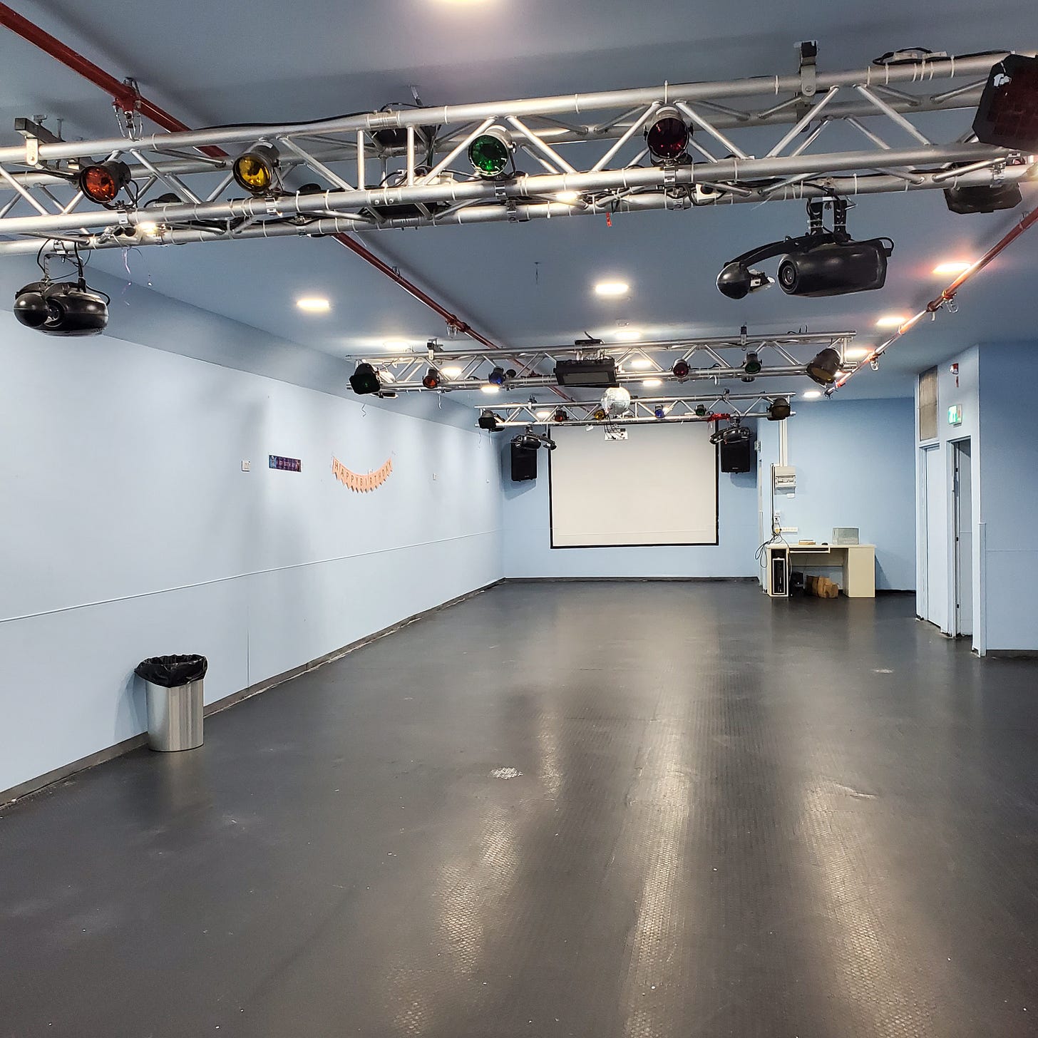 A bare room except for theater lighting, a large whiteboard, and a paper "happy birthday" sign. 
