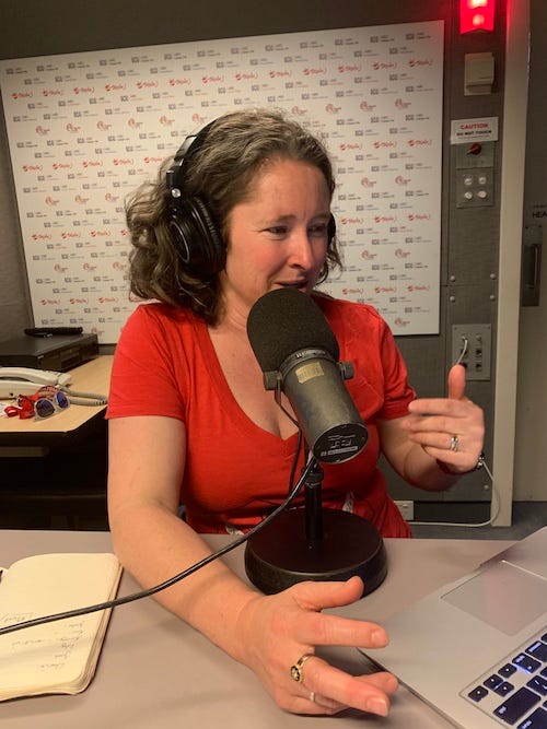 Woman with curly hair speaking into a radio microphone with a computer in front of her