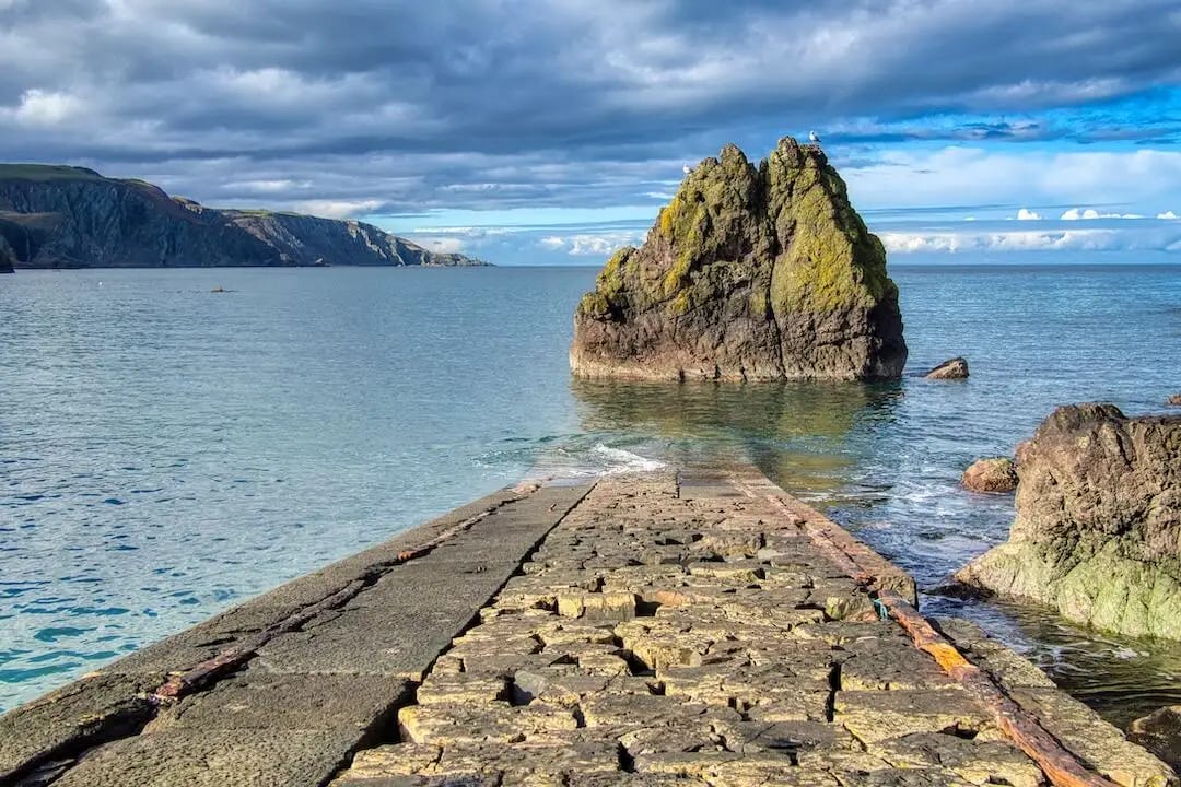 A disused harbour pier disappears into the sea