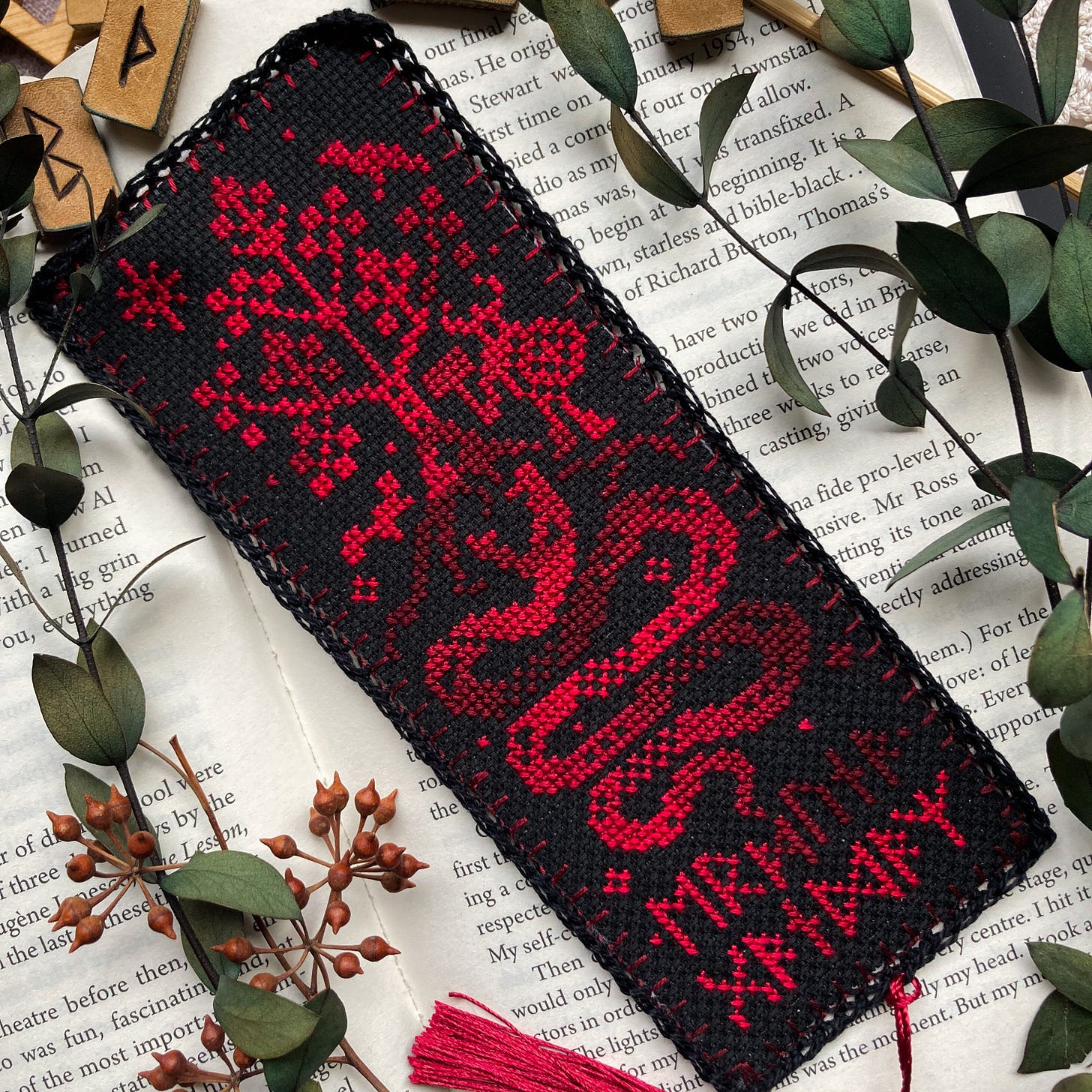 A completed cross stitch bookmark on black fabric, depicting a coiled serpent, a tree, and Thor.