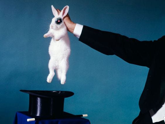 This may contain: a man in a tuxedo is holding up a white rabbit on top of a magician's hat
