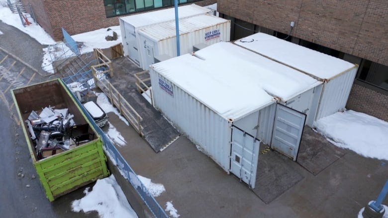 Five white trucking containers are placed on a concrete slab. A green dumpster is next to them. Five white trucking containers are placed on a concrete slab. A green dumpster is next to them.