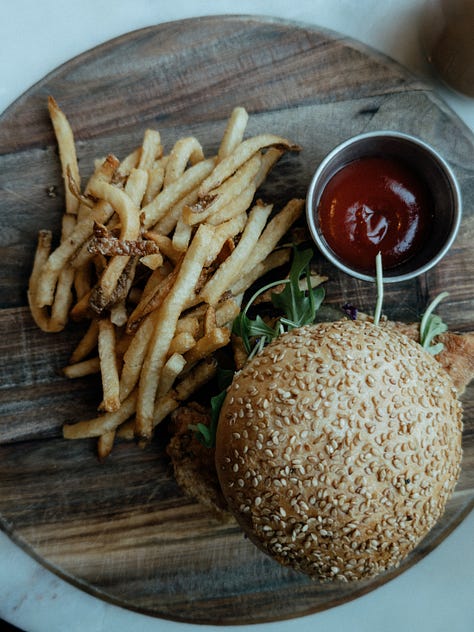 First image: A boat moving through water toward an opening in a gate. Image two: A bookshelf packed with various books. Image three: Overhead view of a wooden serving tray with a burger, cup of ketchup, and fries.