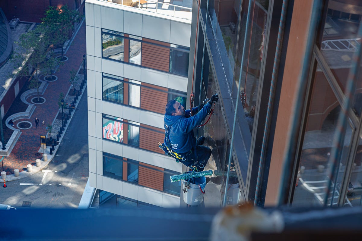Window washer seen from the bedroom side window, dangling mid-wipe.