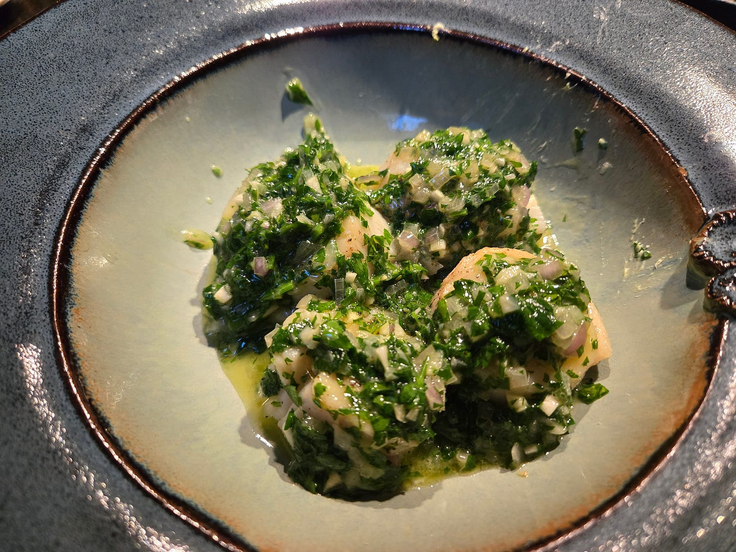 A bowl with four scallops completely covered in parsley, shallot, garlic compound butter with melted butter pooled around.