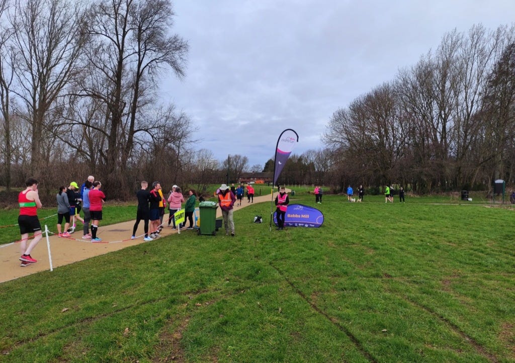 A grassy area next to the start on the path. A parkrun flag and start banner are on the grass.