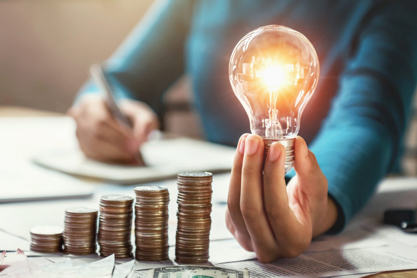 Stacks of coins increasing in height beside a glowing lightbulb, symbolizing smart financial planning and tax strategy for real estate agents.