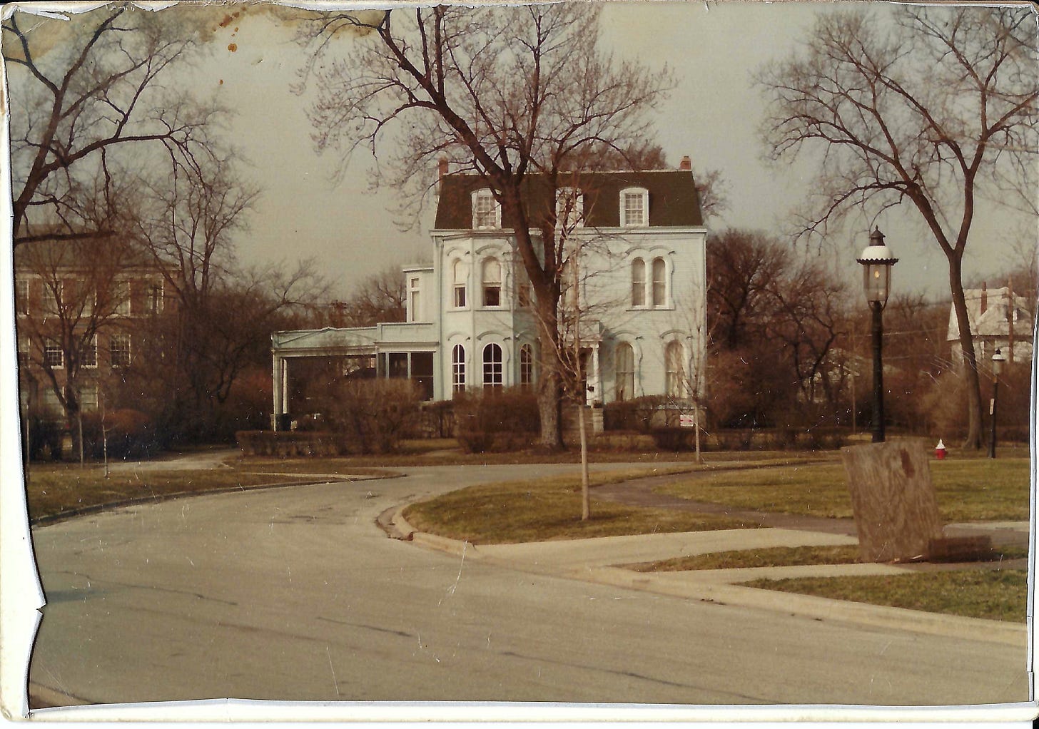 Three-story Victorian house painted light blue with green shingles. Street, bare trees, and gas streetlight in foreground. Three-story Victorian house painted light blue with green shingles. Street, bare trees, and gas streetlight in foreground.
