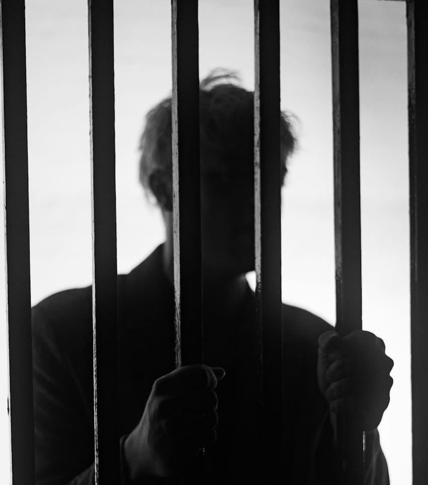 a man standing behind bars in a jail cell a man standing behind bars in a jail cell