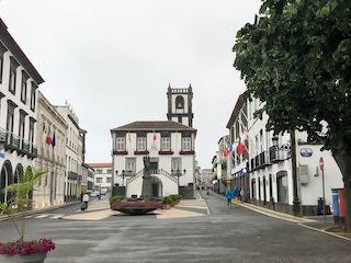 Photos of a sweeping view of an island with an emerald green lake, a plaza in Punta Delgada with a white chuch and white buildings trimmed in brown, a plant-filled tunnel going into a cave.
