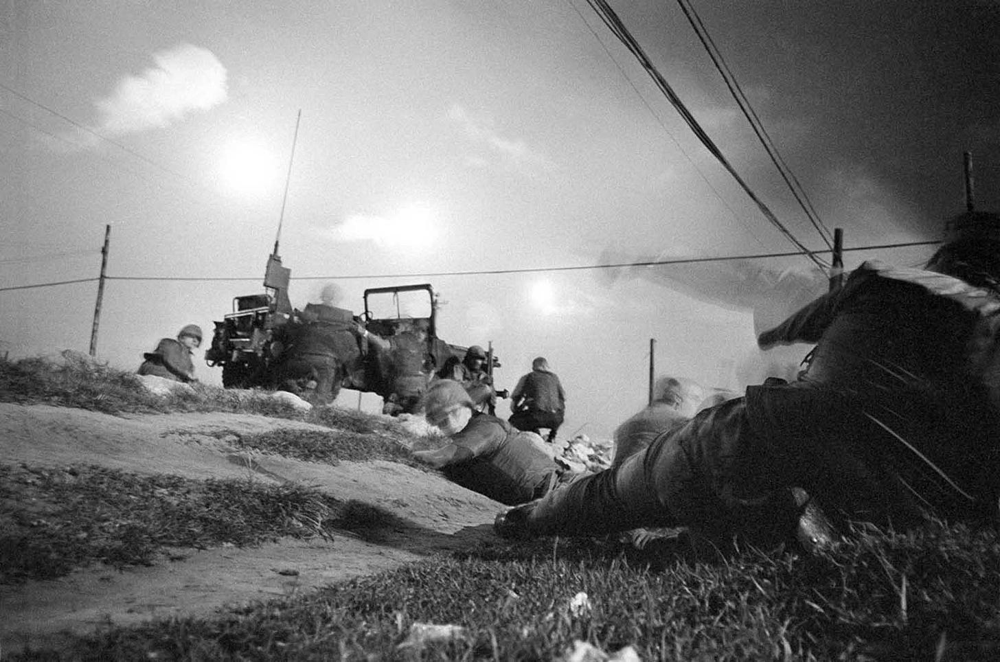 January 30, 1968: U.S. air policemen take cover during sniper fire near Da Nang Airbase, illuminated by flares after a rocket barrage as they hunt for infiltrating Viet Cong guerrillas.