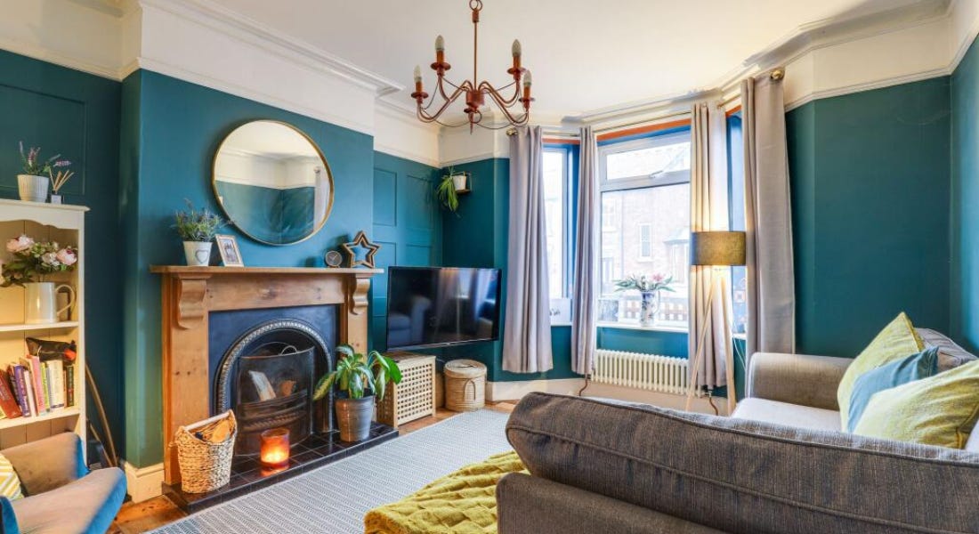 A living room with teal coloured panelling, a fireplace, a grey sofa, and a copper chandelier
