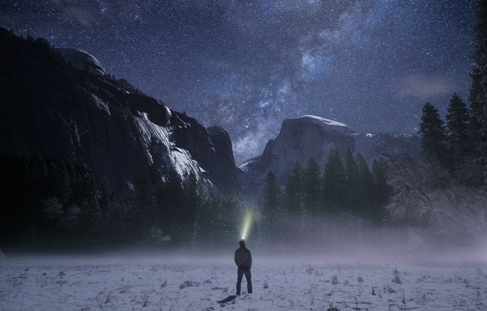 person wearing headlamp facing towards snow mountain person wearing headlamp facing towards snow mountain