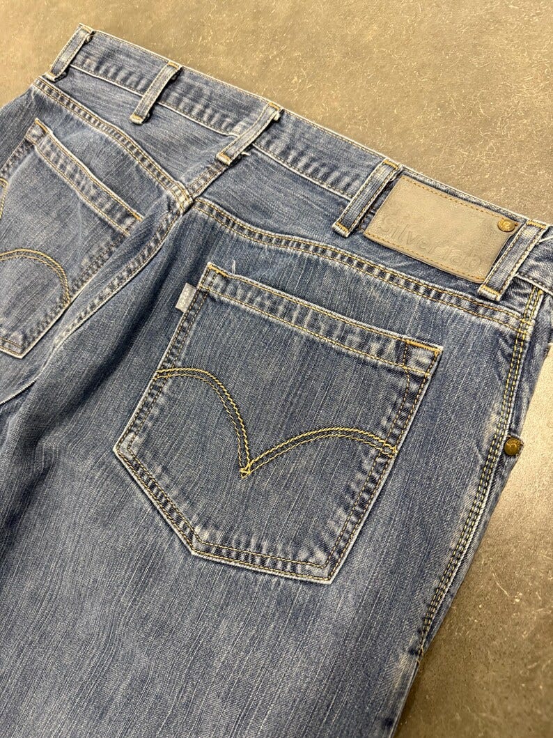 May include: A pair of blue denim jeans with a brown leather patch on the back pocket that says 'Silver Tab'.
