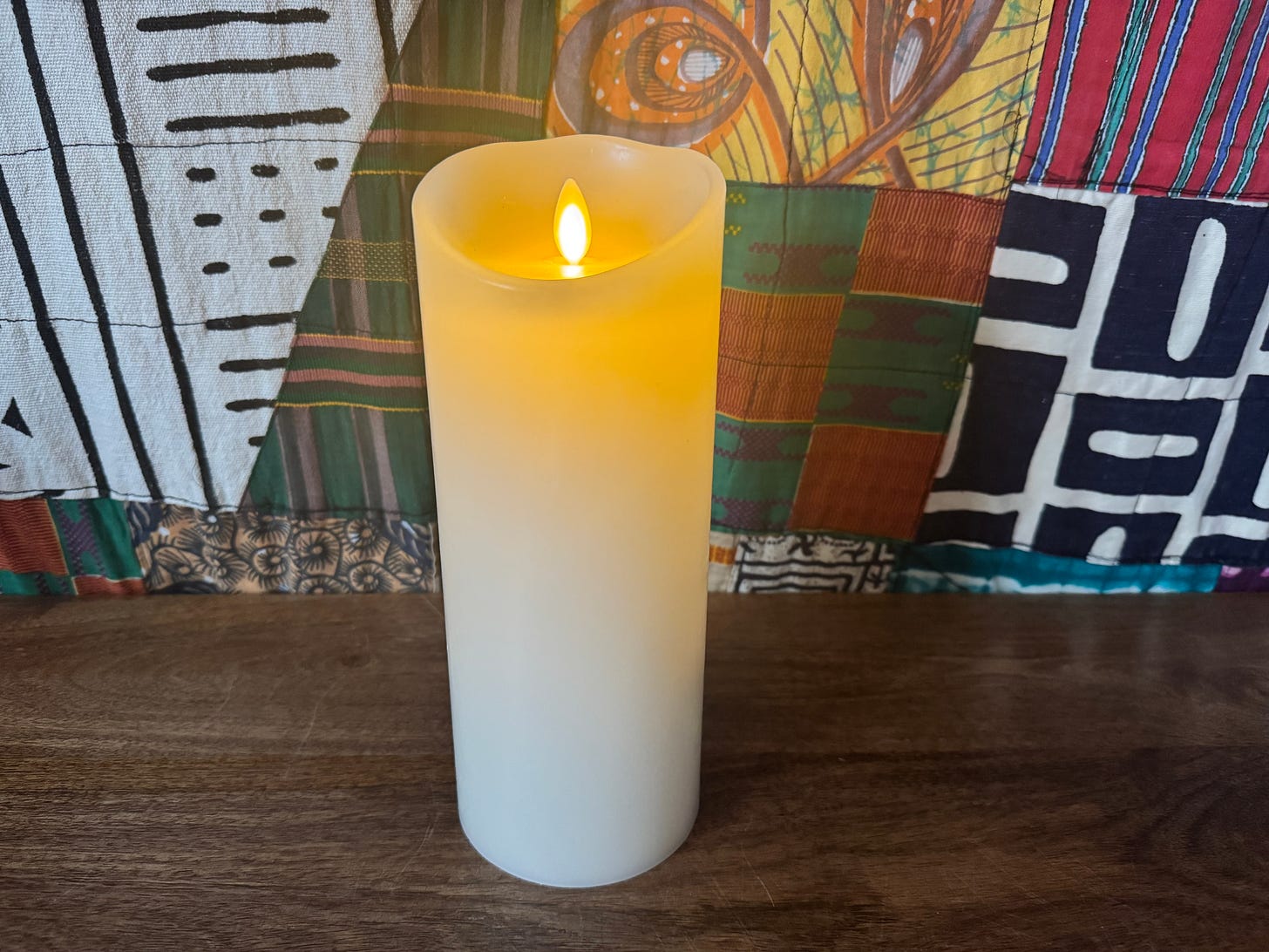 Image of a white lit candle on a wooden cabinet, with a portion of a large mud-cloth quilt visible in the background. Photo courtesy of the author. Image of a white lit candle on a wooden cabinet, with a portion of a large mud-cloth quilt visible in the background. Photo courtesy of the author.