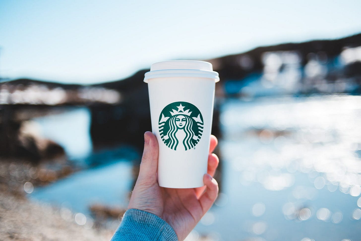 person holding white and green disposable cup person holding white and green disposable cup