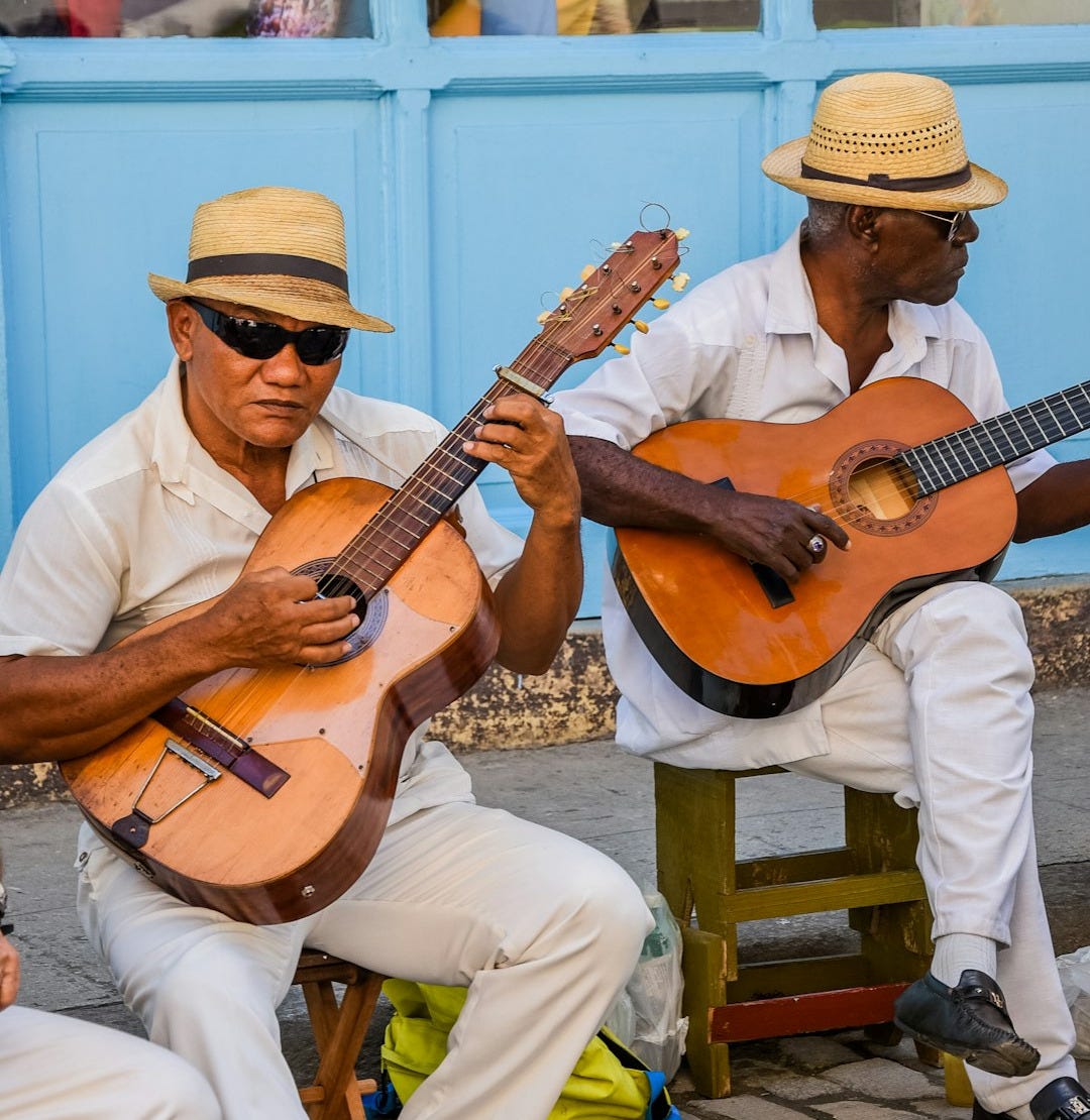 two men sitting on a bench playing guitars two men sitting on a bench playing guitars