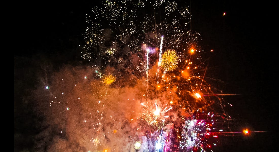 A collection of orange, yellow, purple, and pink fireworks with the night sky behind them