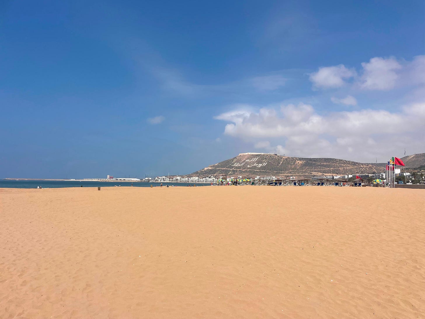 Wide open sand on the beach in front of a mountain that says God, Homeland, King in Arabic