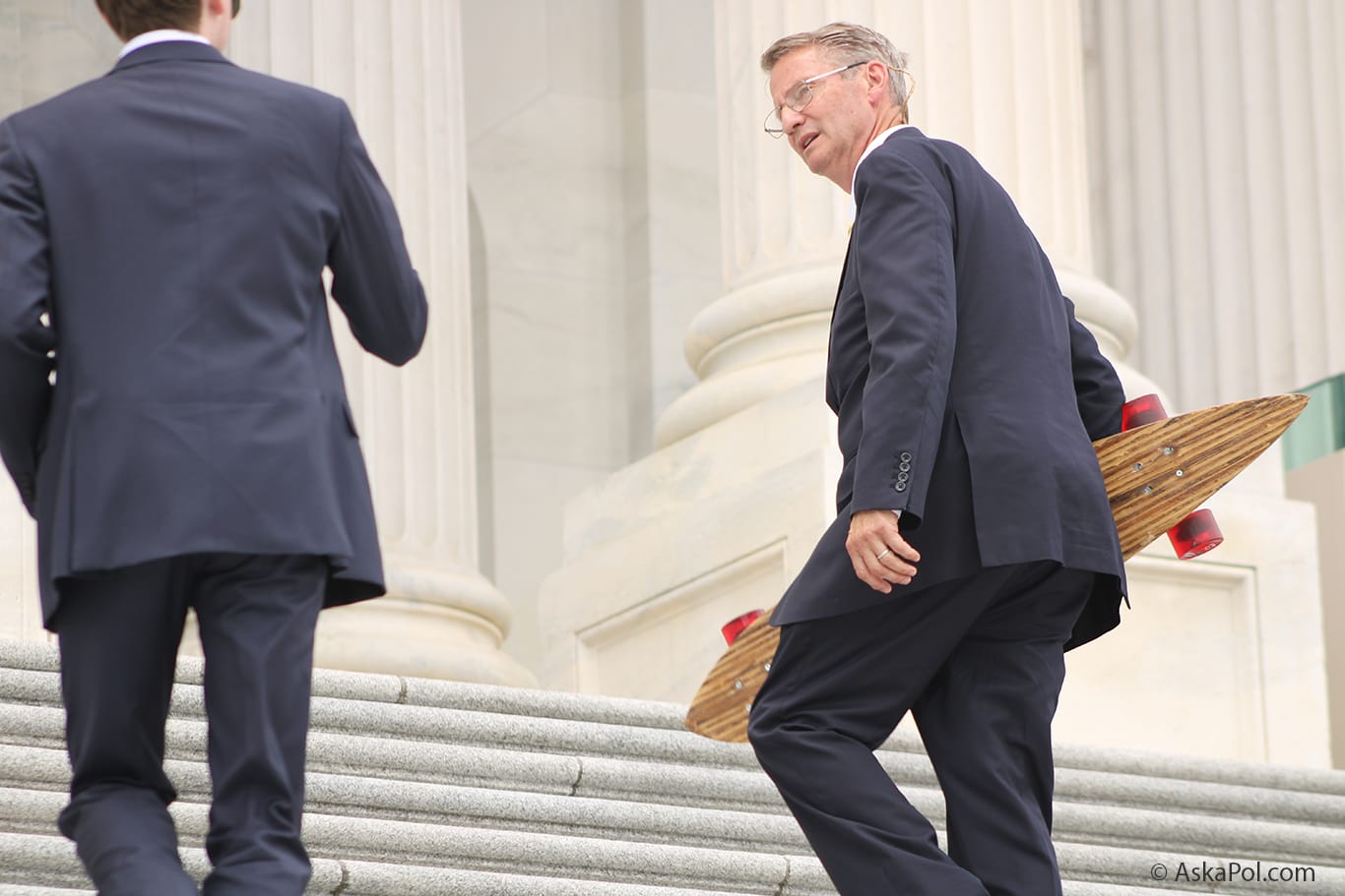 Man in a suit and glasses carries a skateboard © AskaPol.com