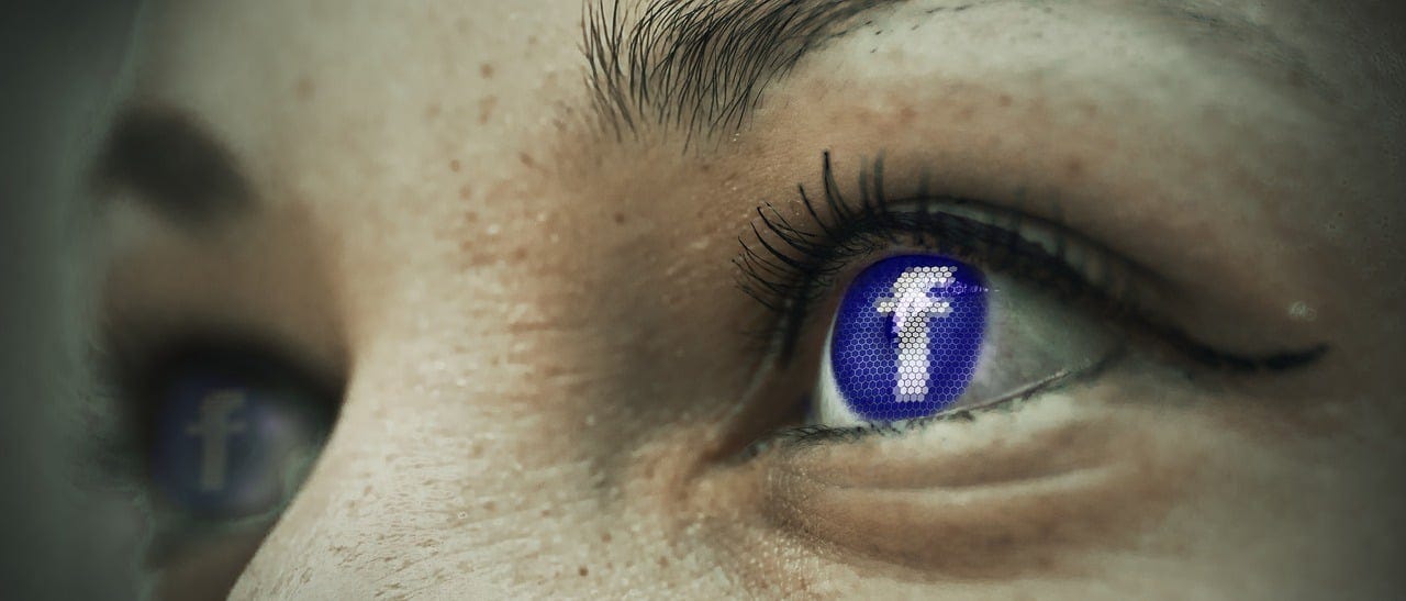 closeup of an eye with Facebook logo in the pupil (social media addiction)