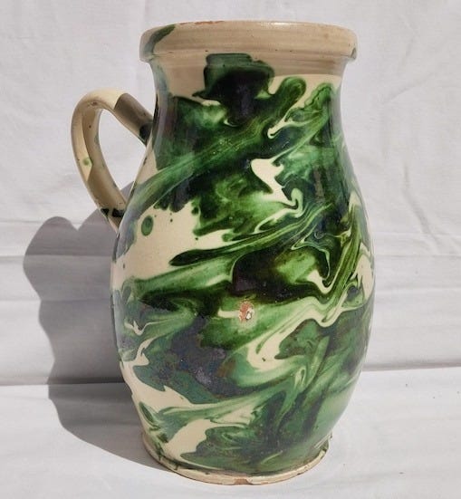 May include: A white ceramic pitcher with a green and white marbled design. The pitcher has a handle and a rounded body.