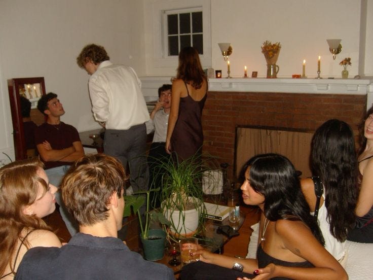 This may contain: a group of young people sitting around a living room with candles on the fire place